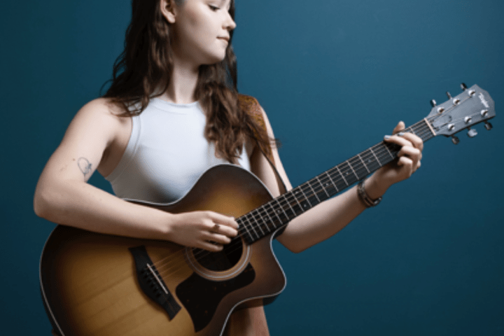 Woman playing an acoustic guitar against a blue background.